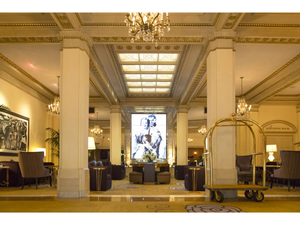 The grand lobby is brought to life with a dazzling chandelier, vibrant artwork, comfortable seating arrangements, and a lobby cart. The space is inviting, ideal for socializing, relaxing, and enjoying refreshments, showcasing the communal luxury and comfort of the hotel's common areas.