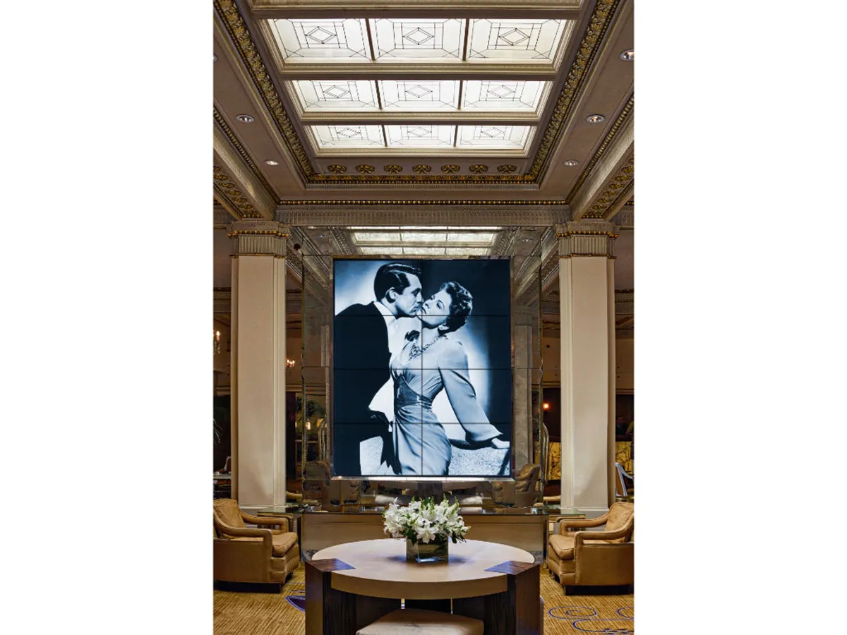 A refined lounge area with a large black-and-white photograph of a couple kissing, a decorative ceiling, and an elegantly arranged coffee table with fresh flowers. Plush armchairs create an intimate, restful space that feels both luxurious and personal.
